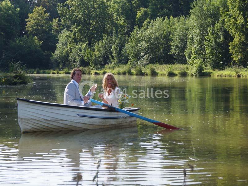 Un couple assis dans une barque sur un lac entouré de végétation, tenant des verres et un bouquet de fleurs.