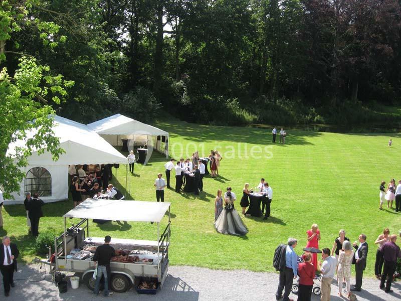 Groupe de personnes rassemblées dans un jardin pour un événement, avec tentes blanches et barbecue en arrière-plan.