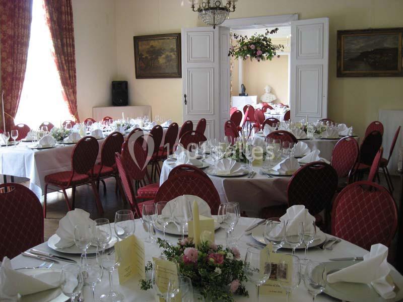 Salle de réception élégamment décorée avec des tables rondes dressées, nappes blanches et chaises rouges.