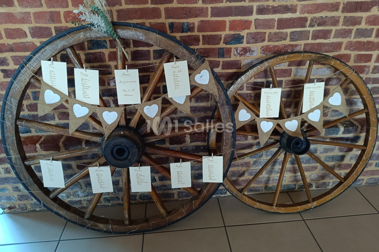 Deux roues en bois décorées de cœurs et de cartons suspendus affichant des noms, posées contre un mur de briques.