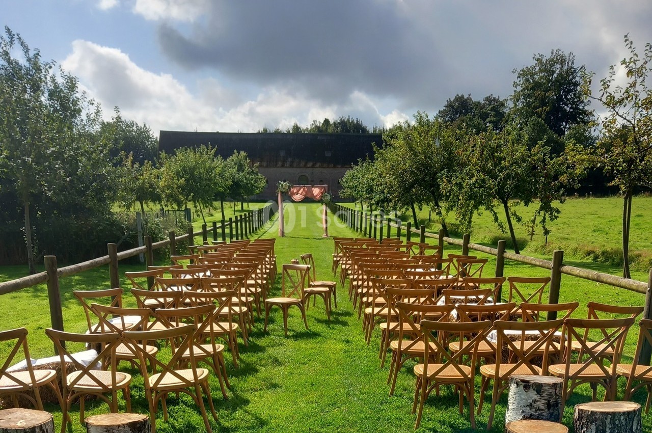 Chaises en bois disposées en rangées sur une pelouse, formant une allée centrale menant à une arche décorative en extérieur.