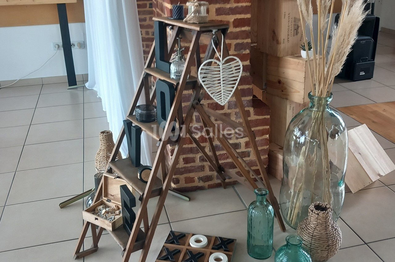 Échelle en bois décorative avec objets en osier, bougies et vases, posée près d'un mur en briques.