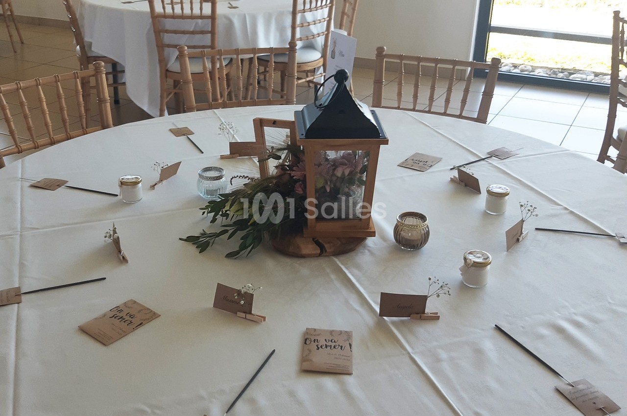 Centre de table avec lanterne, fleurs et bougies, entouré de marque-places sur une table ronde dressée.