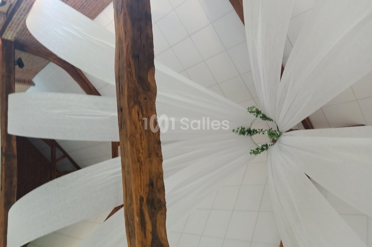 Plafond décoré de voilages blancs suspendus à des poutres en bois, avec des branches vertes au centre.