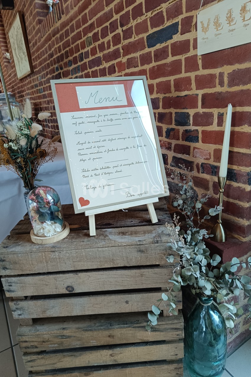 Ardoise de menu manuscrite posée sur une caisse en bois, entourée de décorations florales et d'objets décoratifs.