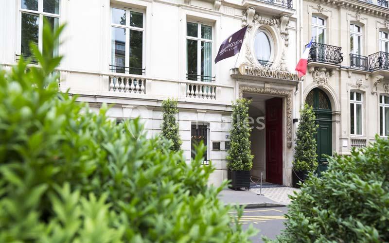 Façade d'un bâtiment élégant avec drapeaux français et européen, entouré de verdure.