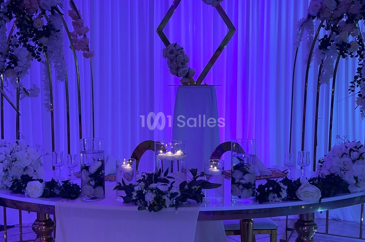 Table décorée pour un événement avec fleurs blanches, bougies allumées et arrière-plan violet illuminé.