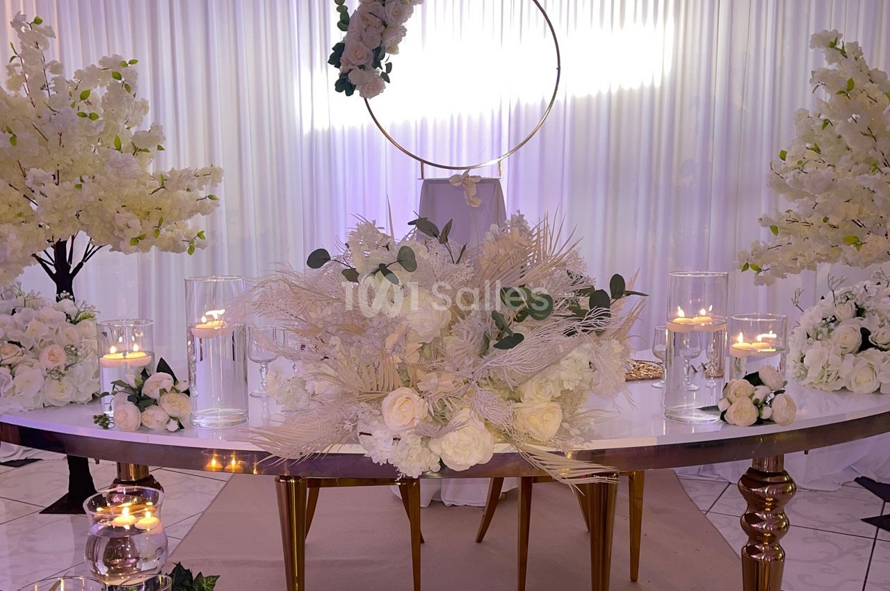 Décoration de table élégante avec fleurs blanches, bougies allumées et arche circulaire ornée de fleurs en arrière-plan.