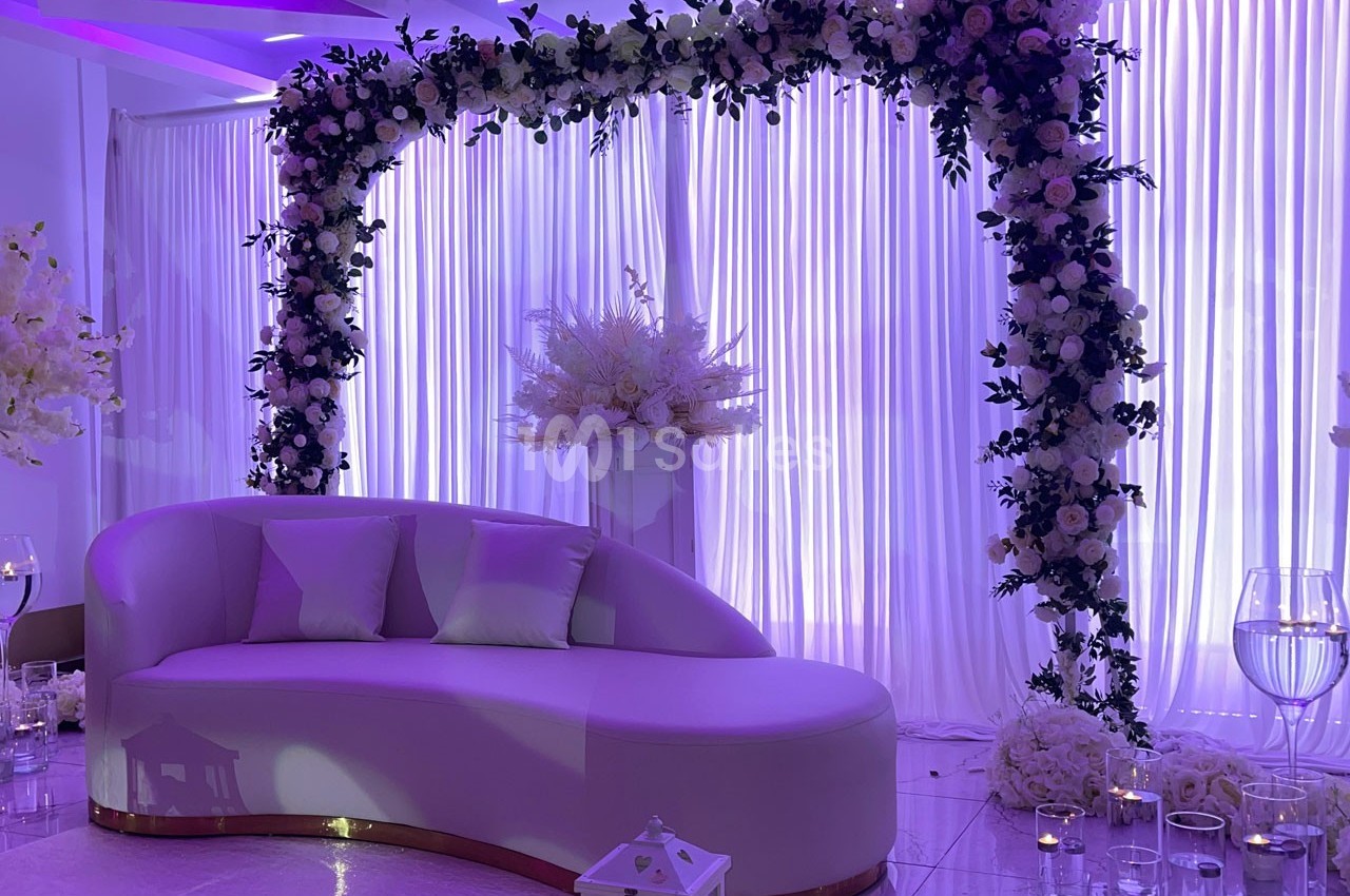 Canapé blanc devant une arche florale ornée de roses et feuillages, éclairée par une lumière violette douce.