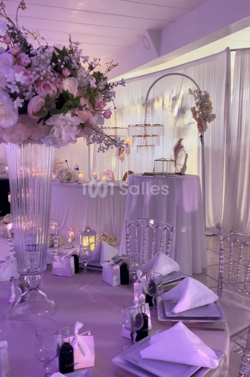 Salle de réception décorée avec des tables élégantes, des fleurs, des chandeliers et un éclairage doux.