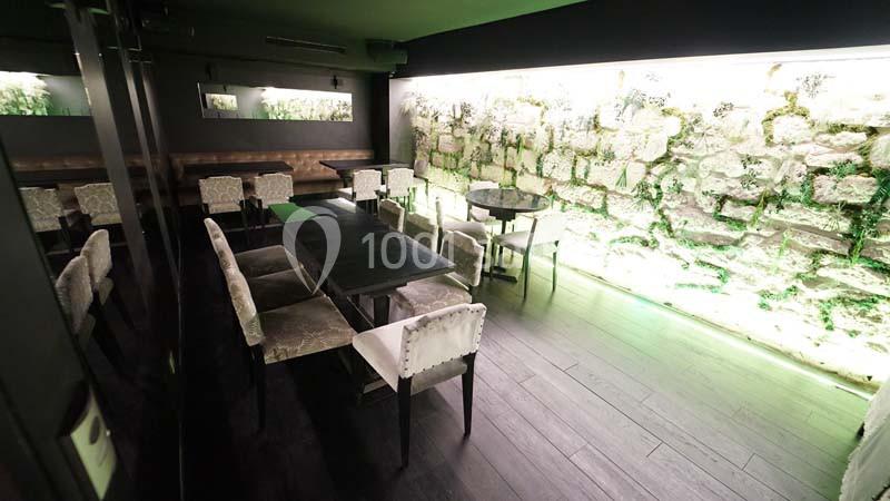 Salle de restaurant moderne avec murs en pierre éclairés, tables noires et chaises claires alignées.