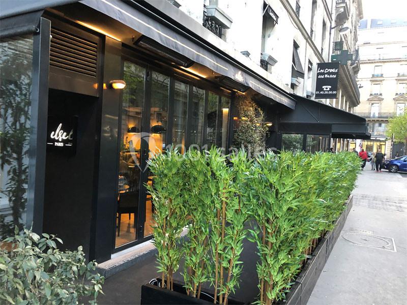 Façade d'un restaurant moderne avec terrasse bordée de plantes vertes dans une rue urbaine.