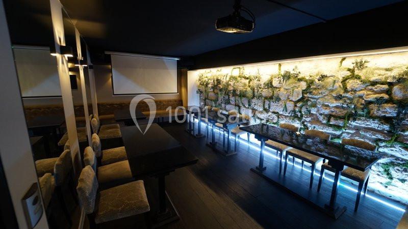 Salle moderne avec tables, chaises rembourrées, mur en pierre végétalisé et éclairage tamisé.