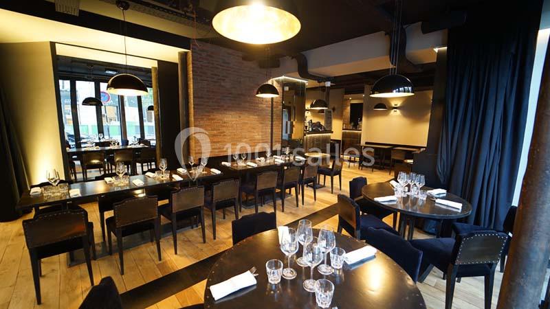 Salle de restaurant moderne avec tables en bois sombre, chaises noires, éclairage suspendu et murs en briques apparentes.