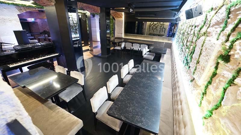Salle moderne avec tables noires, chaises claires, murs en pierre ornés de verdure et éclairage tamisé.