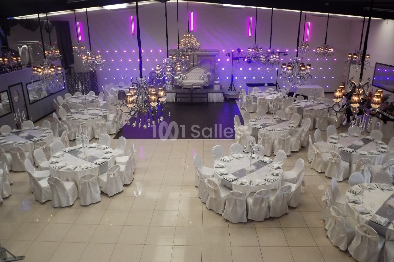 Salle de réception élégante avec tables rondes dressées, chaises blanches et éclairage décoratif violet.