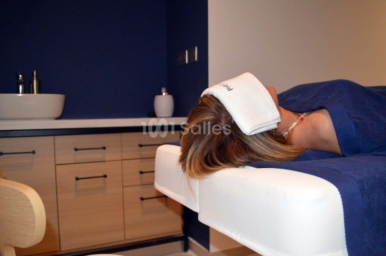 Femme allongée sur une table de massage dans une pièce au décor épuré avec lavabo et meubles en bois clair.