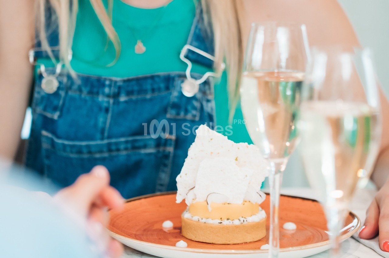 Une personne devant une tartelette garnie de meringue, entourée de verres de champagne sur une table.