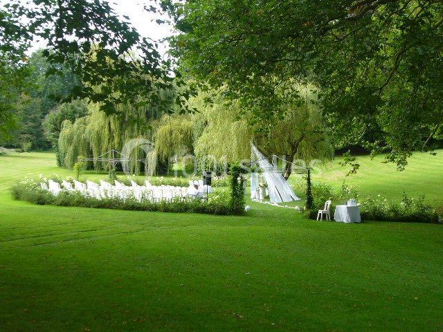 Chaises blanches disposées en extérieur sous des arbres, avec une tente et une table dans un cadre verdoyant.