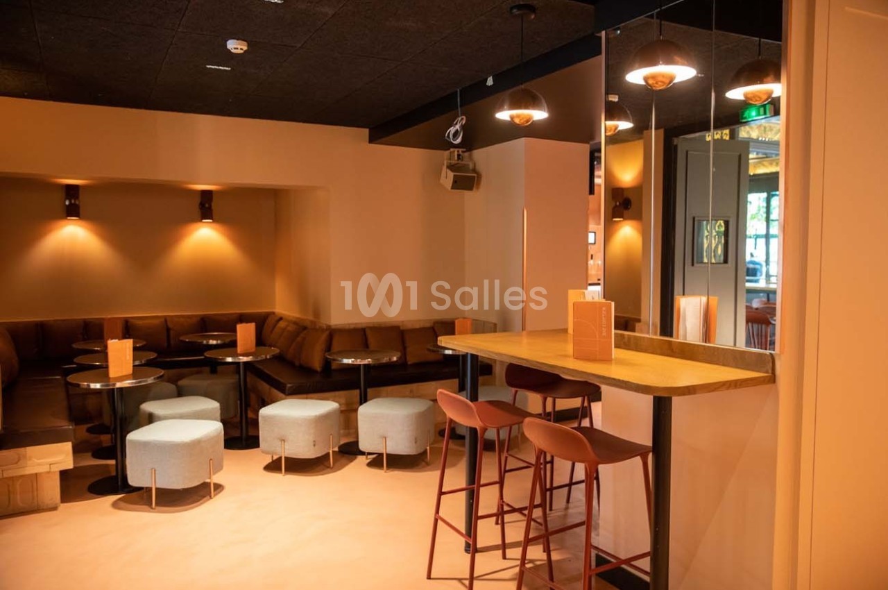 Espace intérieur moderne avec tables basses, tabourets, banquettes et éclairage tamisé.