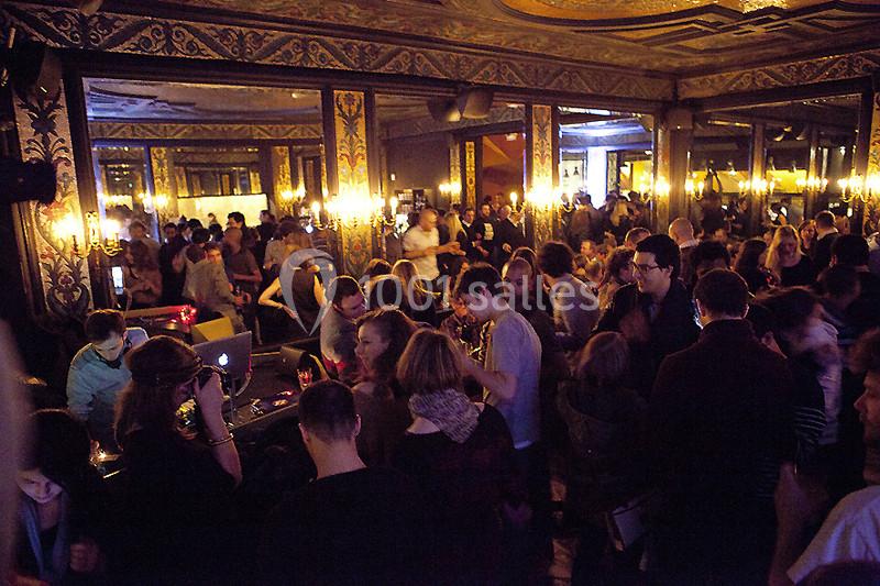 Groupe de personnes dans une salle ornée de miroirs et de lustres, avec un DJ jouant de la musique en arrière-plan.