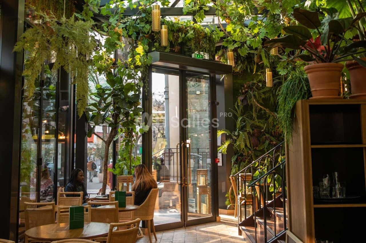 Intérieur d'un café lumineux avec des plantes suspendues, des tables en bois et de grandes baies vitrées donnant sur l…