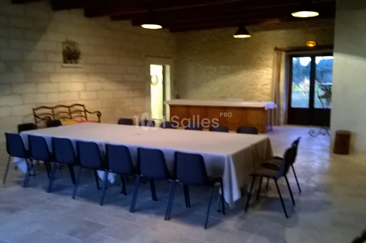 Salle avec une grande table rectangulaire recouverte d'une nappe blanche, entourée de chaises noires, éclairée par des…