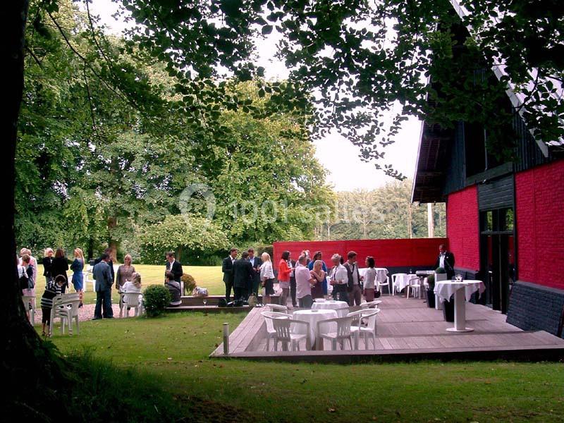 Groupe de personnes rassemblées sur une terrasse en bois près d'un bâtiment rouge, entourée de verdure.
