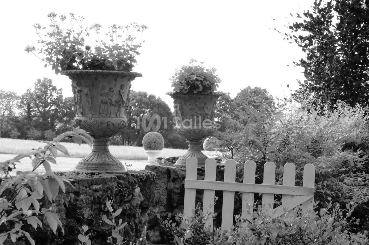 Deux jardinières sculptées sur un muret en pierre, entourées de végétation, avec une petite barrière en bois.