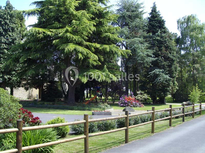 Espace vert avec arbres, fleurs colorées, aire de jeux et clôture en bois le long d'une allée pavée.