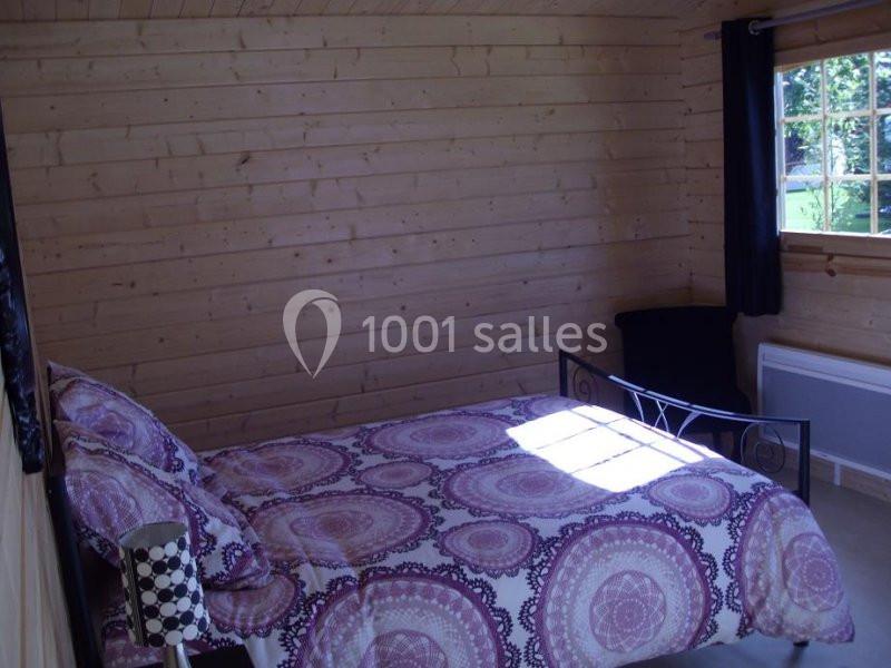 Chambre en bois avec lit double à motif violet, lampe de chevet, fenêtre donnant sur un extérieur verdoyant.