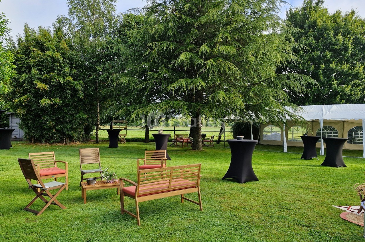 Mobilier de jardin en bois disposé sur une pelouse, entouré d'arbres, avec des tables hautes et une tente blanche en arrière…
