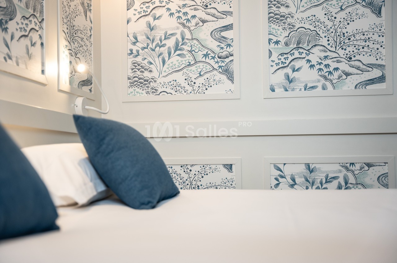 Lit avec oreillers bleus dans une chambre décorée de panneaux muraux illustrés de motifs végétaux bleus et blancs.