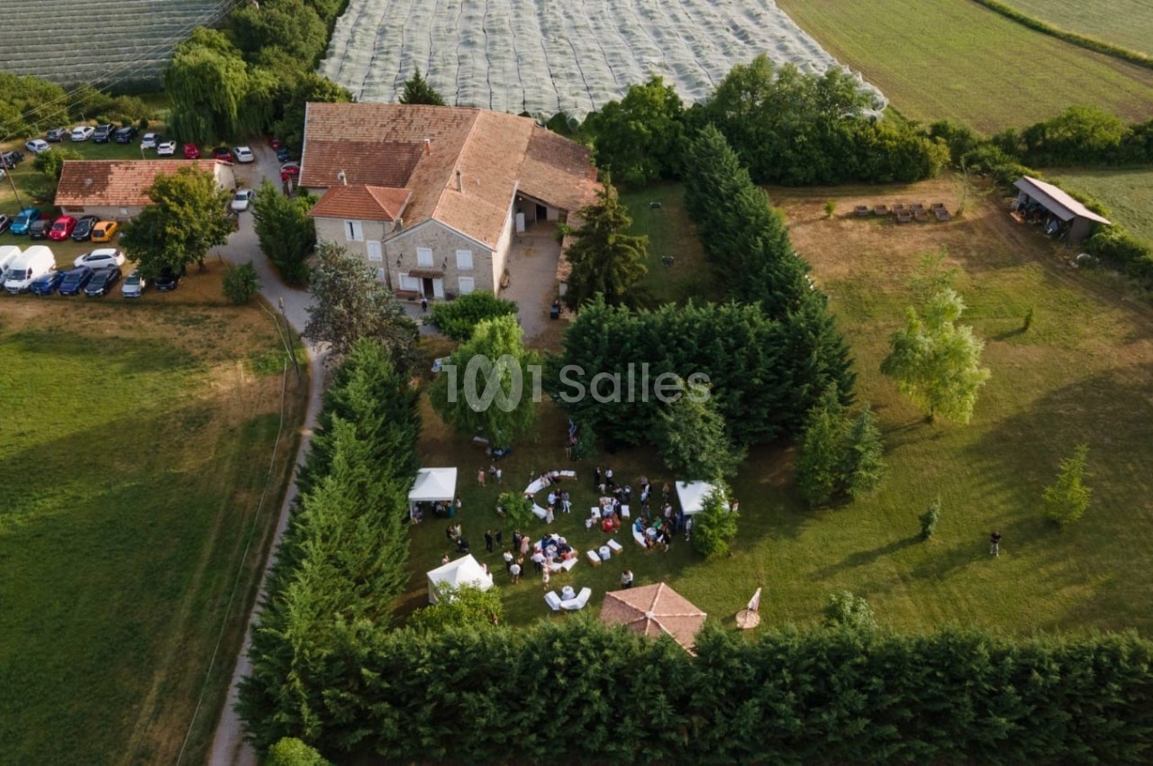 Vue aérienne d'une maison entourée de jardins, avec des invités réunis sous des tentes dans un cadre champêtre.