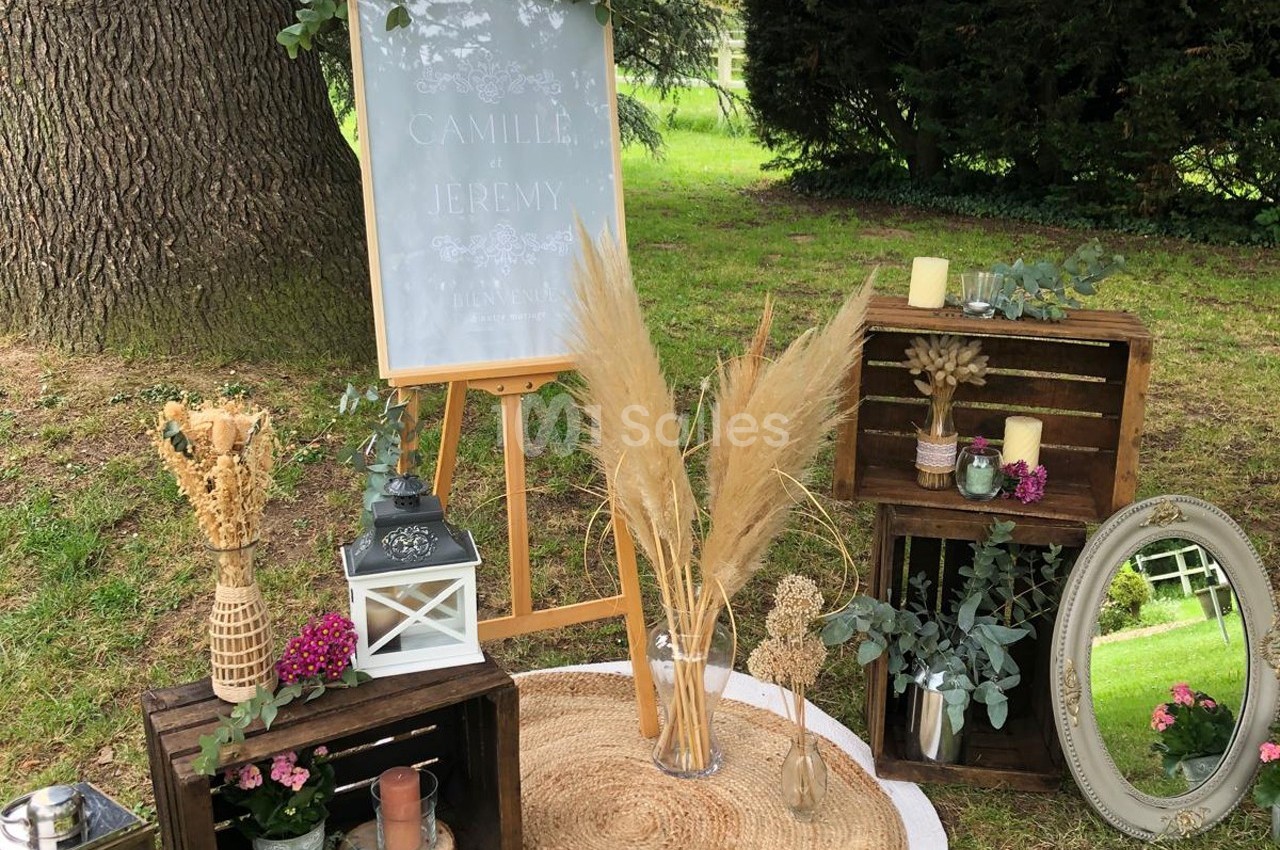 Décoration champêtre avec fleurs séchées, lanternes, miroirs et caisses en bois disposés sur un tapis en extérieur.