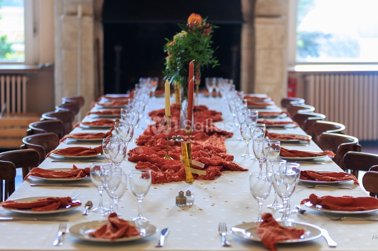 Grande table dressée avec nappes blanches, serviettes rouges, verres et couverts, décorée de bougies et fleurs au centre.