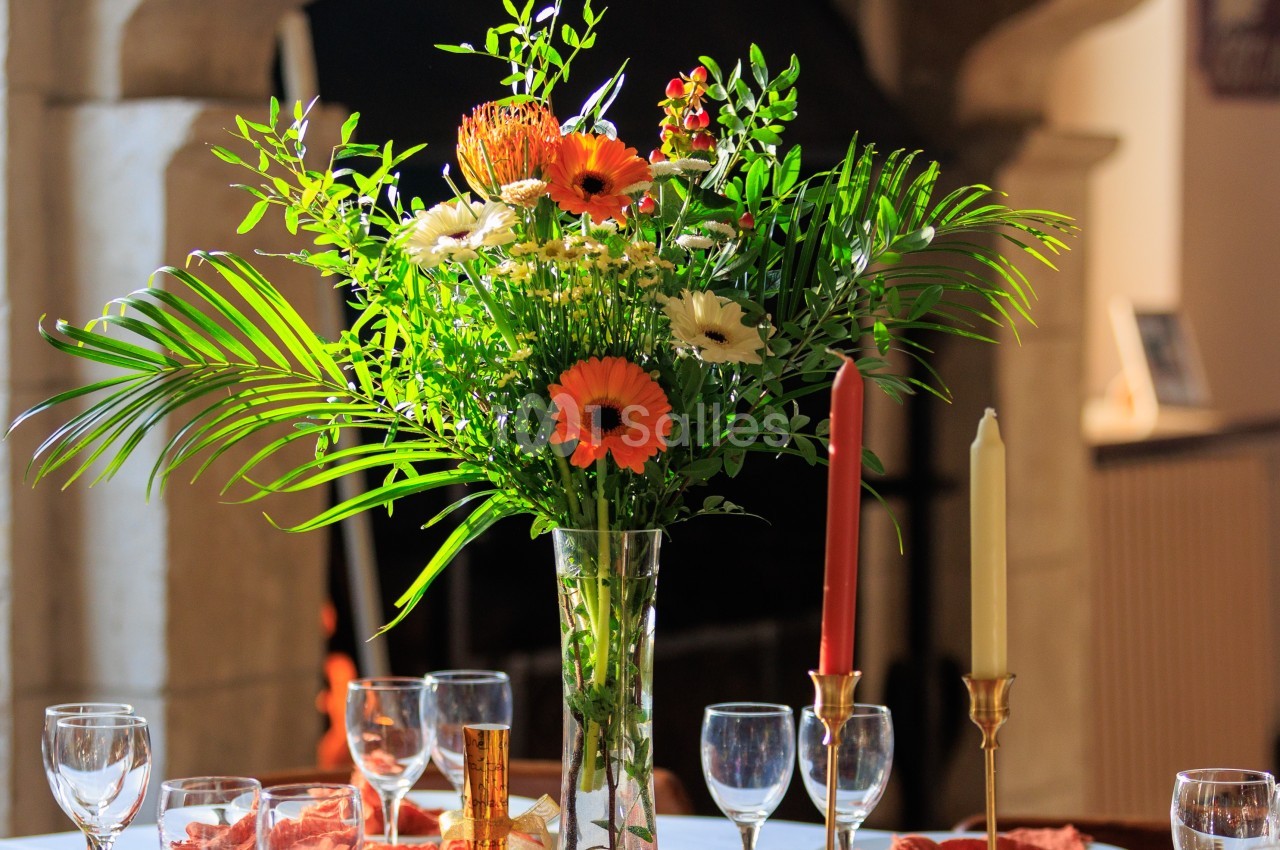 Bouquet de fleurs colorées dans un vase en verre, posé sur une table dressée avec des verres et des bougeoirs.