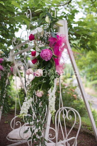 Décoration florale composée de roses, pivoines et feuillage, accrochée à une structure blanche en extérieur.