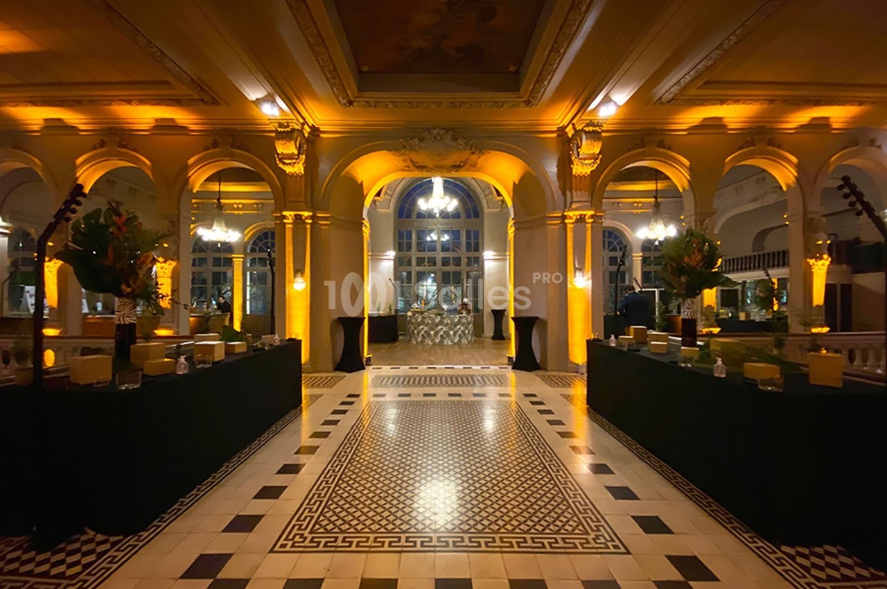Hall spacieux avec sol en mosaïque, arches illuminées et tables décorées, éclairage chaleureux et ambiance élégante.