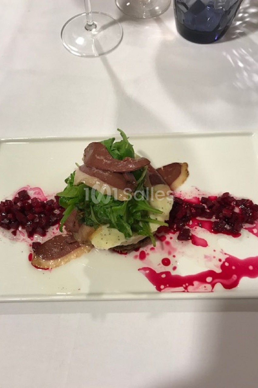 Assiette gastronomique avec salade, tranches de viande, betterave en dés et sauce colorée sur une table dressée.
