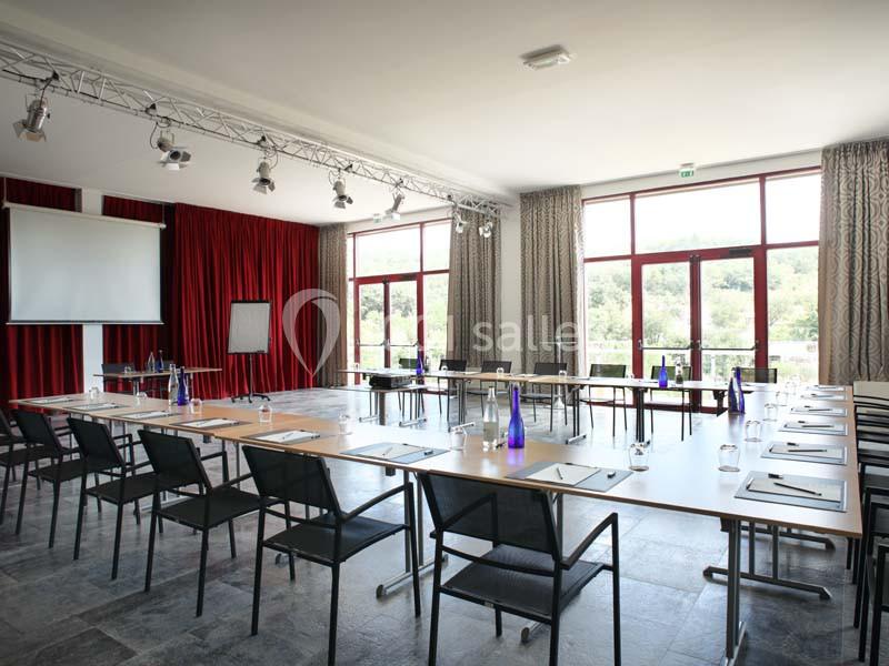 Salle de réunion lumineuse avec tables disposées en U, chaises noires, écran de projection et grandes fenêtres donnant sur…