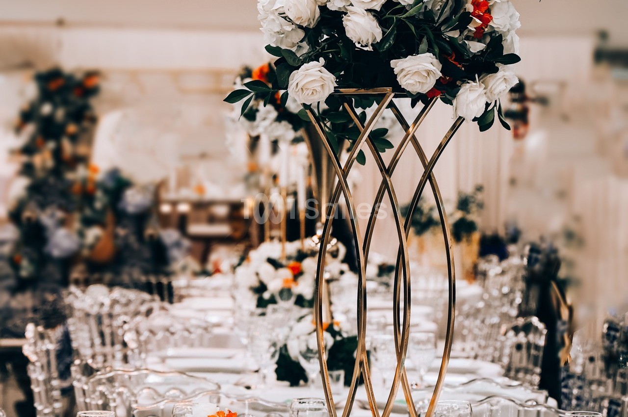 Centre de table floral avec roses blanches et touches d'orange, entouré de chaises transparentes et d'une décoration…