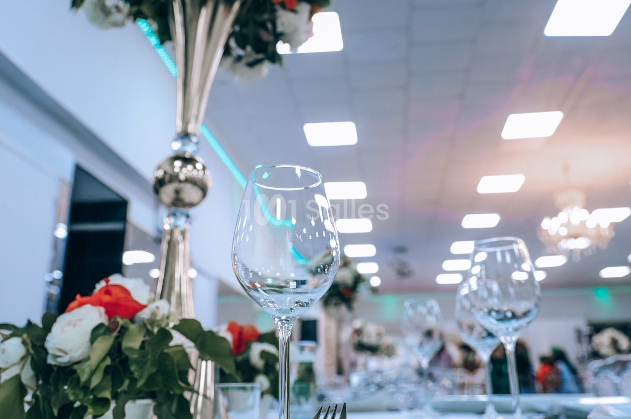 Verres à pied et compositions florales sur une table élégamment dressée dans une salle lumineuse.