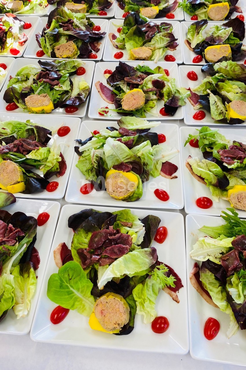Assiettes de salade garnies de feuilles vertes, tomates cerises, tranches de viande séchée et rondelles de terrine.