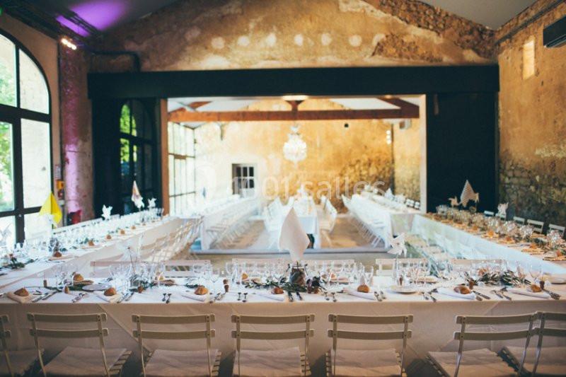 Salle de réception avec de longues tables dressées pour un banquet, décorée dans un style rustique et lumineux.