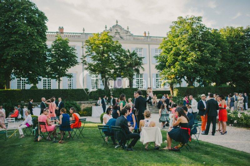 Personnes réunies dans un jardin devant un bâtiment élégant, discutant et profitant d'une réception en plein air.