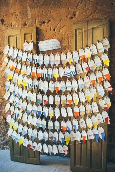 Des enveloppes colorées suspendues sur des cordes devant un mur en pierre et des panneaux en bois.