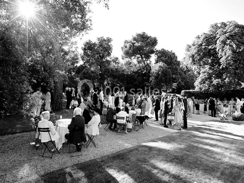 Groupe de personnes rassemblées dans un jardin pour un événement, assises ou debout sous un ciel ensoleillé.