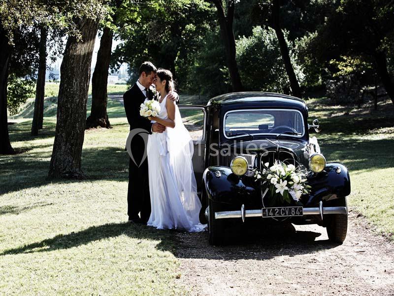 Un couple de mariés pose près d'une voiture ancienne décorée de fleurs dans un parc verdoyant.