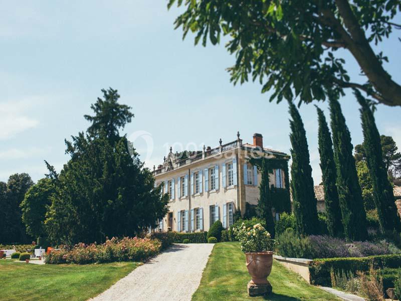 Allée gravillonnée menant à une grande maison entourée de jardins paysagers avec arbres et arbustes.